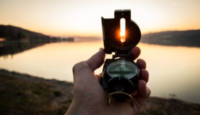 A hand holding a compass overlooking a lake in the sunset